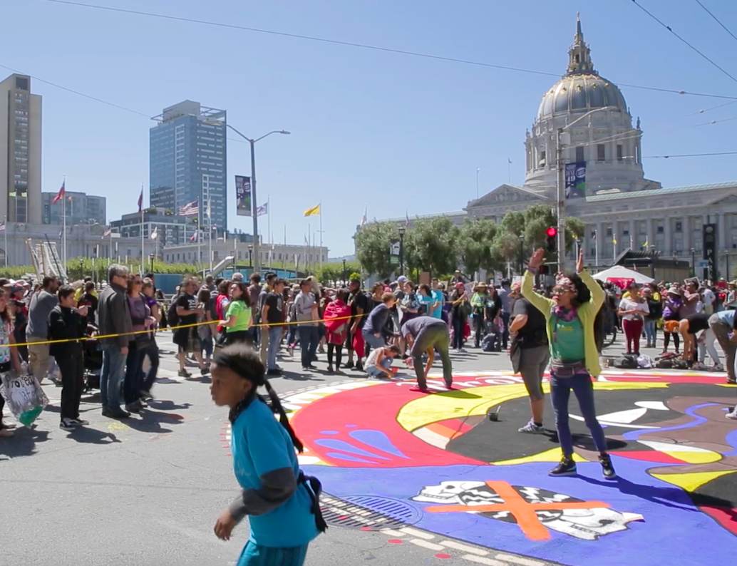 A diverse crowd of individuals standing around a vibrant, painted circle.