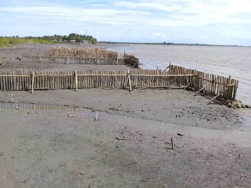 A wooden fence submerged in water near a sandy beach.