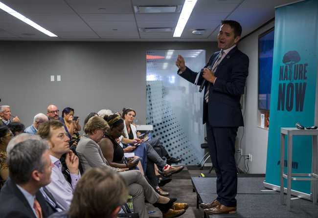 A professional man in formal attire addressing a large audience during a corporate event.