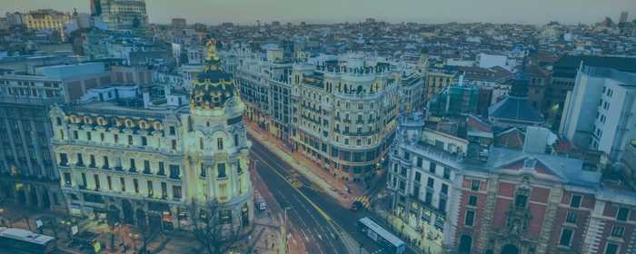 Aerial view of Madrid cityscape with buildings, streets, and parks under a clear blue sky.