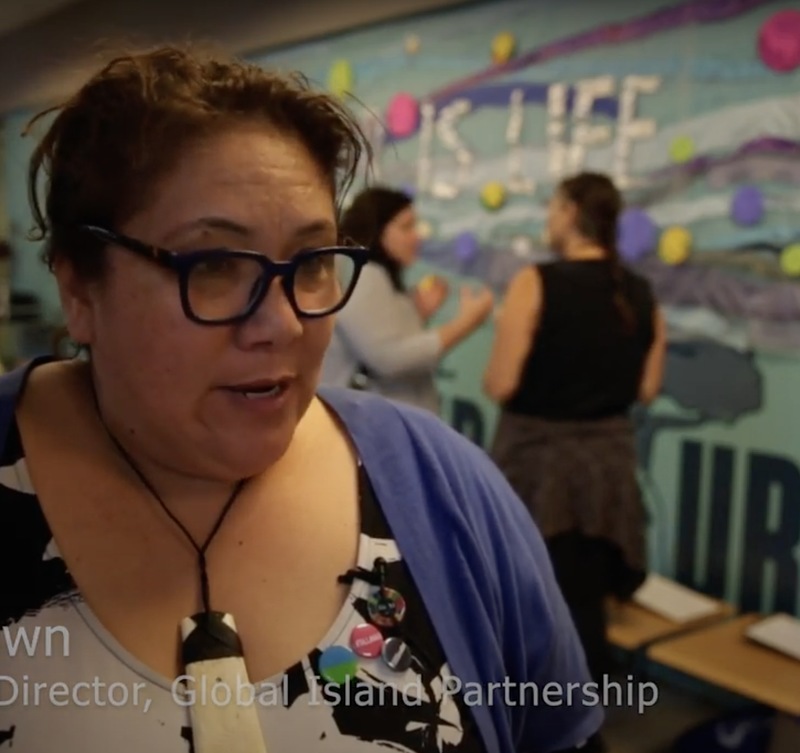 A woman wearing glasses and a blue shirt stands confidently, exuding a professional demeanor.