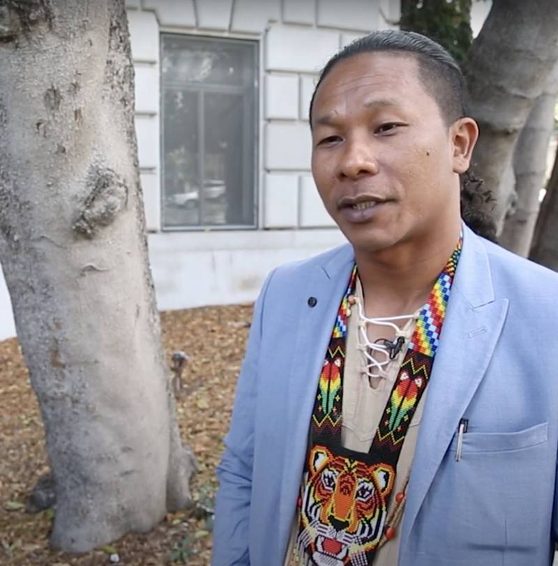 A man adorned in a handwoven necklace and a stylish jacket, showcasing a unique and colorful fashion statement.