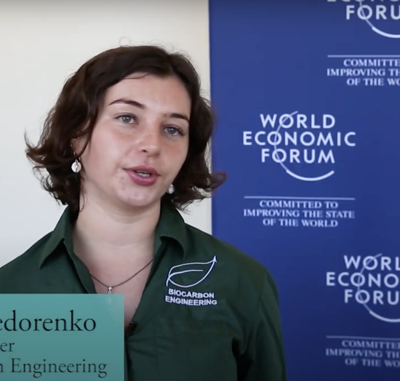 The woman wearing a green shirt is smiling and talking directly to the camera.