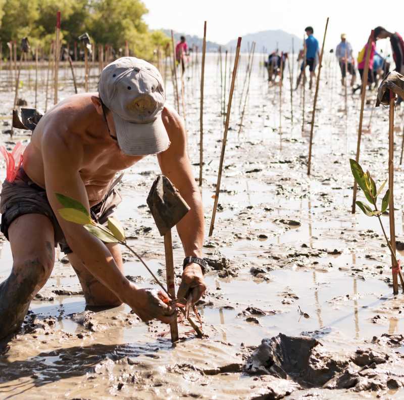 A man kneels in the mud, his figure partially obscured by the surrounding earth, evoking a sense of humility.