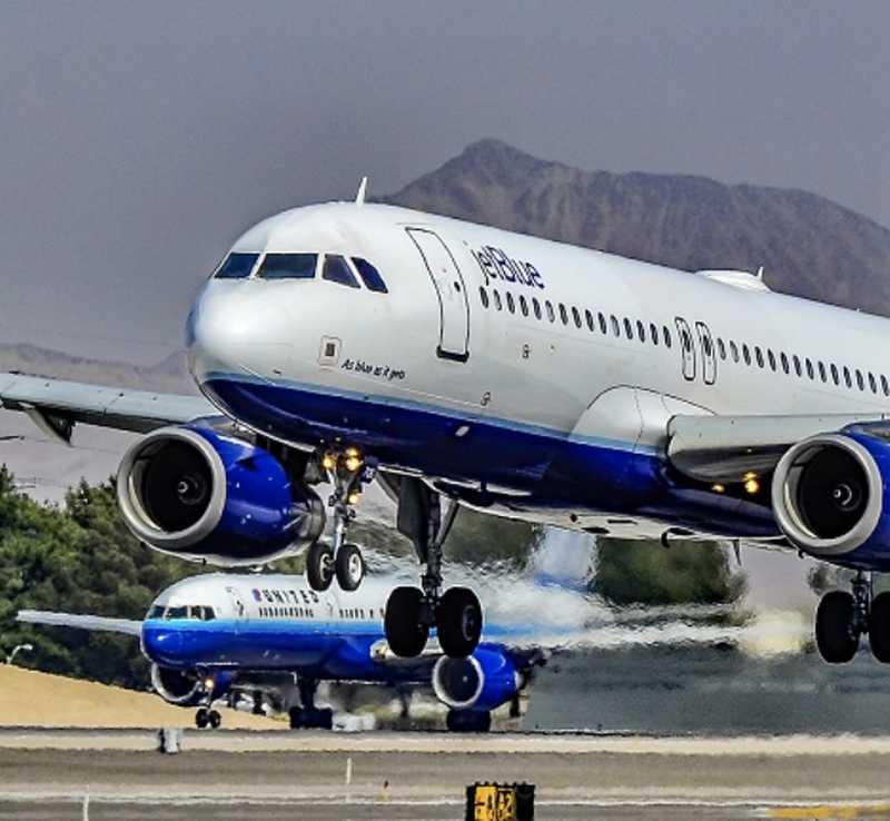 Pair of aircrafts lifting off runway, with wheels retracting into fuselage.