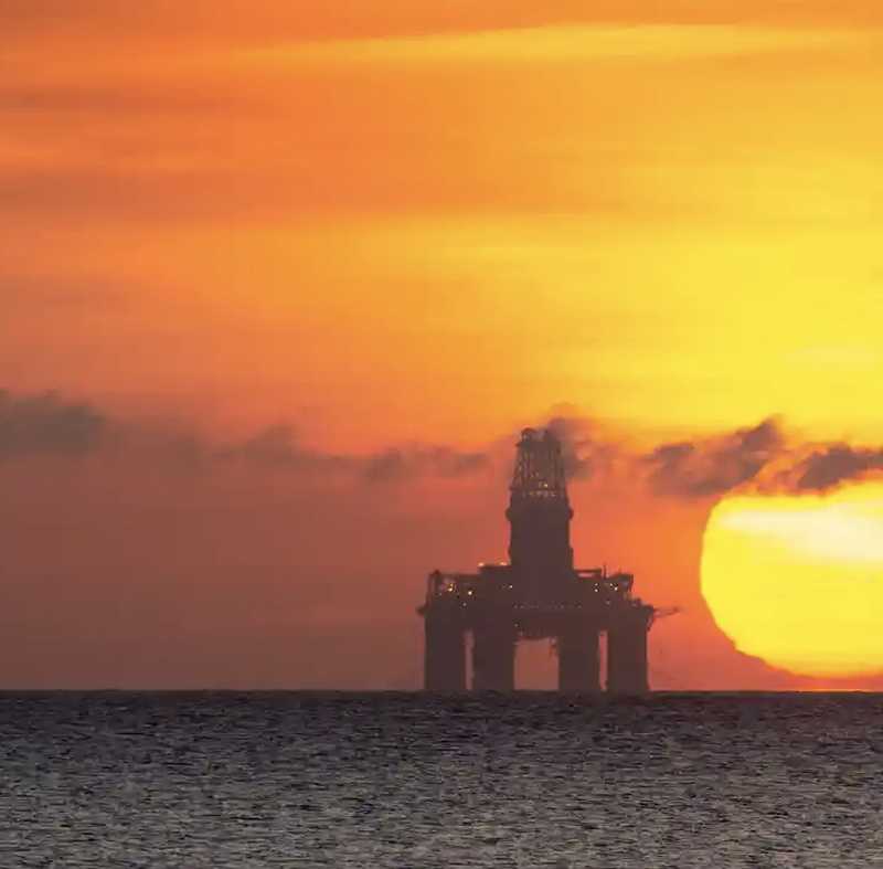 Industrial oil rig under a colorful sunset sky.