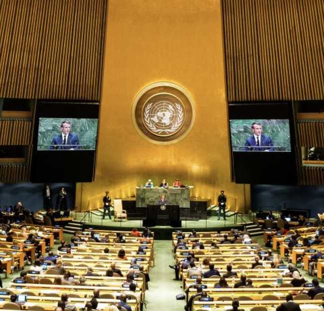 A wide shot of the UN General Assembly in session, with delegates gathered in a large room.